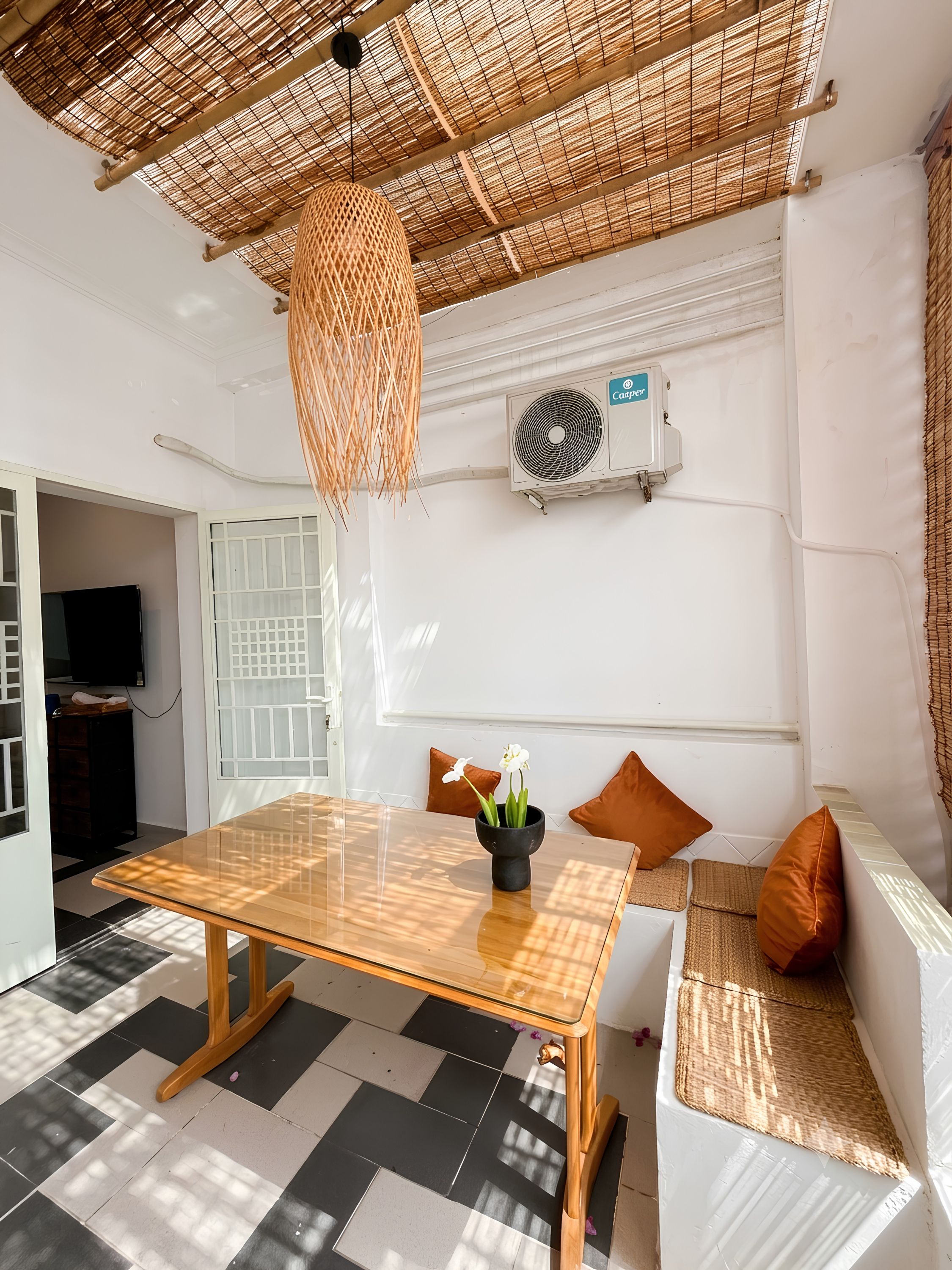 A room with a checkered floor, a wooden table with a vase of flowers, a sofa with cushions, a hanging light fixture, and an air conditioning unit.