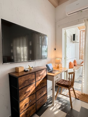 Una habitación moderna con televisión de pantalla plana, escritorio de madera, computadora portátil y una silla cómoda.