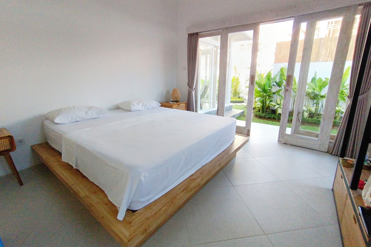 A bedroom with a wooden bed, a nightstand, and a view of a garden through a sliding glass door.