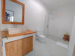 A modern bathroom with a wooden vanity, a large mirror, a toilet, and a glass-enclosed shower. - Dimora Bali Residence (Badung)