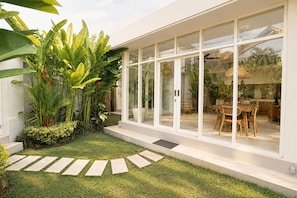 A modern house with a glass door leading to a dining area, surrounded by lush greenery. - Dimora Bali Residence (Badung)