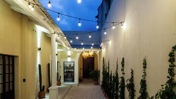 Un pasillo con luces colgantes, plantas en macetas y vistas a una habitación con una puerta al final.