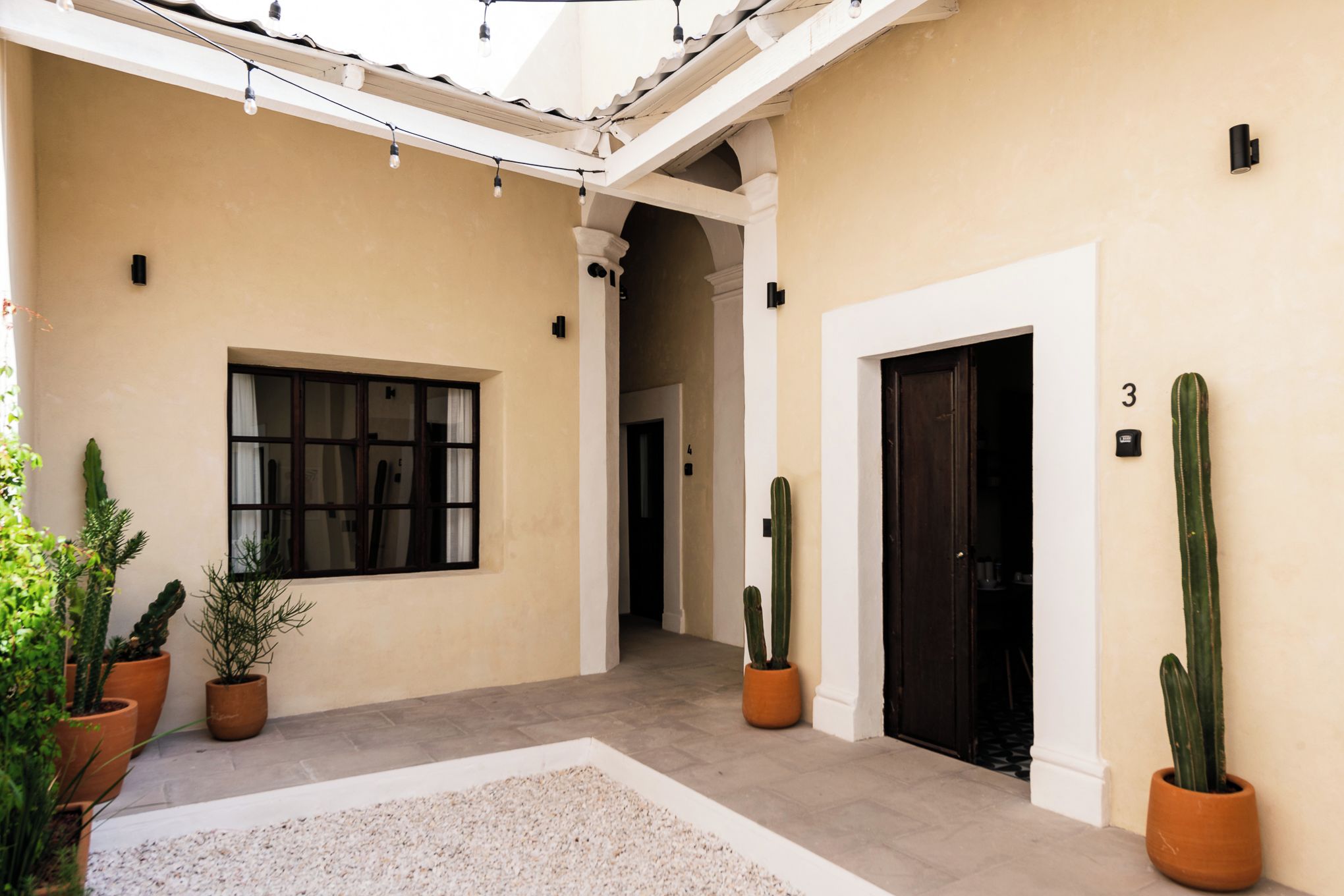 Un patio con suelo de baldosas, plantas en macetas, una ventana y una puerta.