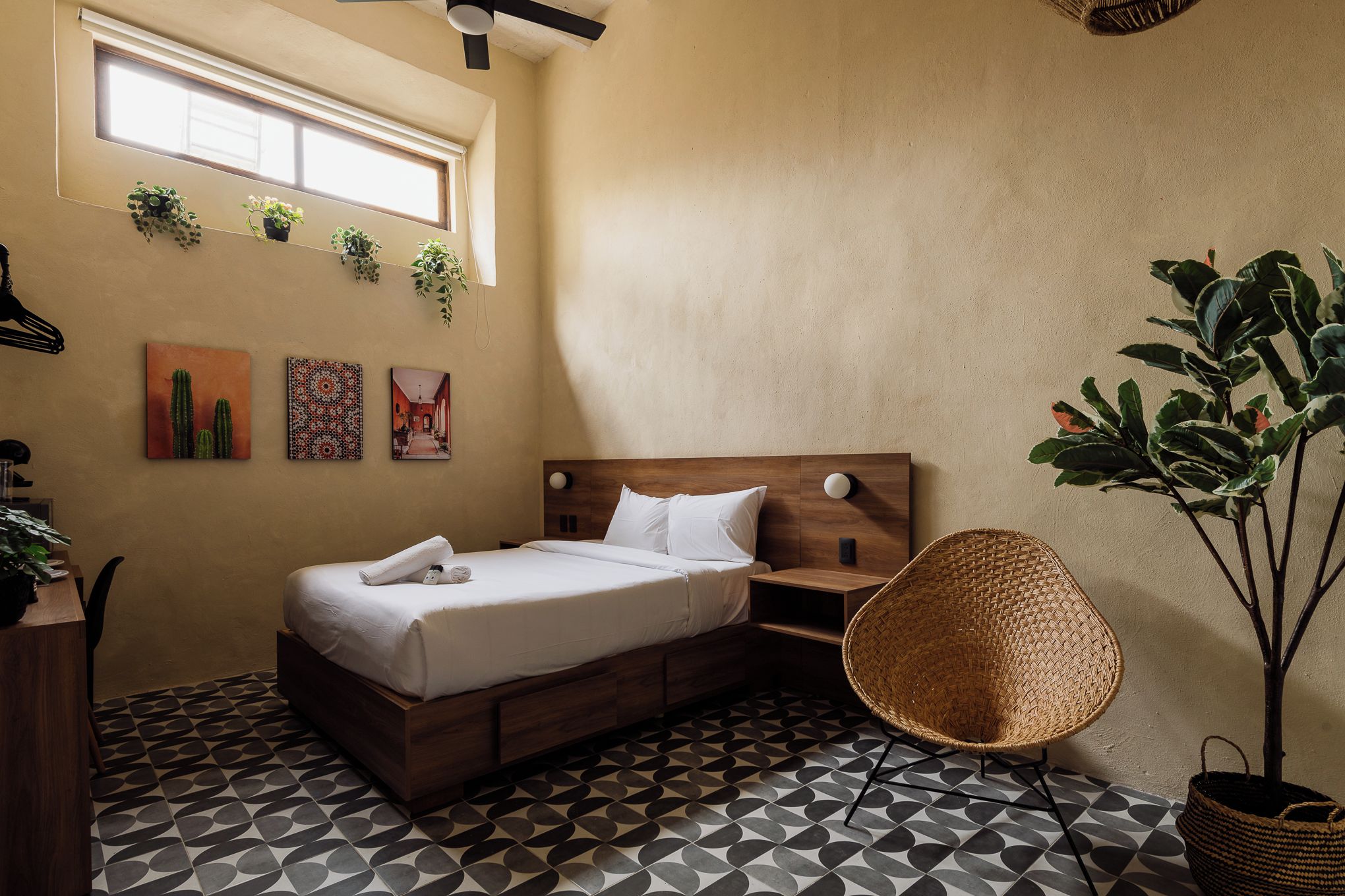 A bedroom with a bed, bedside table, wall art, and a potted plant.