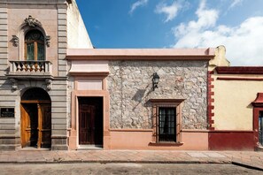 A building with a stone facade, a wooden door, and a small window with a metal grille. - Hidalgo By Homirent (Santiago de Querétaro)