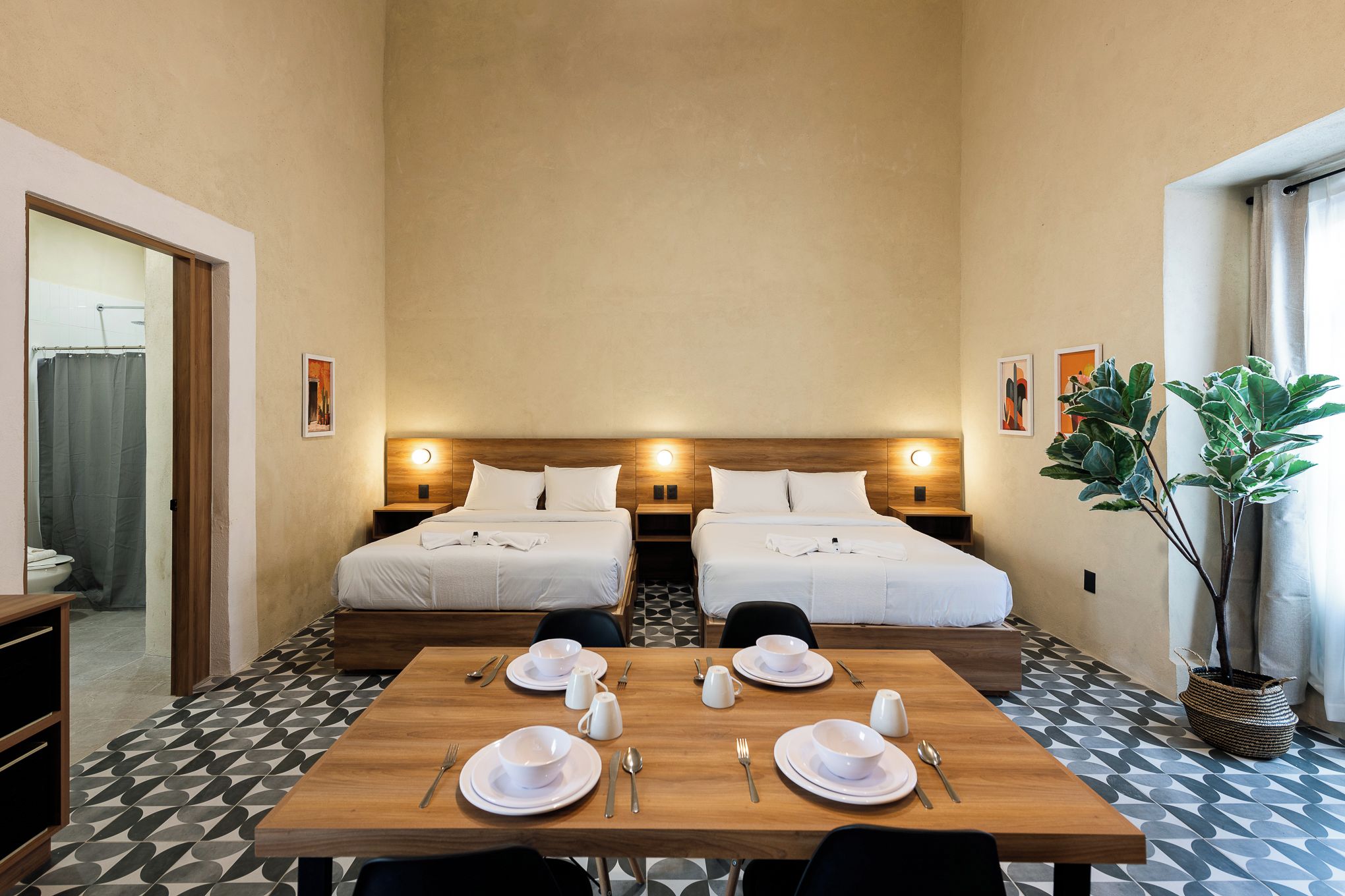 Ein Hotelzimmer mit zwei Betten, einem Esstisch für zwei Personen und einer großen Topfpflanze.