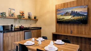 A modern kitchen with a dining area, a flat-screen TV mounted on the wall, and a painting above the TV.