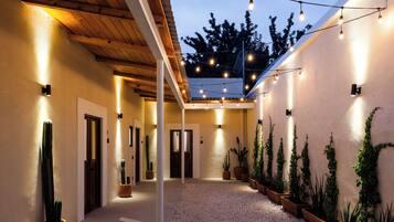 Un corredor exterior cubierto con luces en el techo, plantas en macetas y suelo de grava.