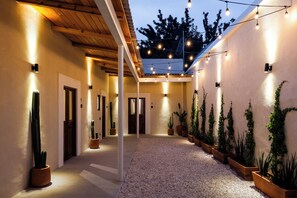 Un corredor exterior cubierto con luces en el techo, plantas en macetas y suelo de grava.