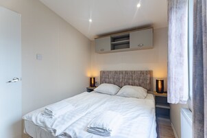 A bedroom with a bed, bedside lamps, a nightstand, a mirror above the bed, and a door.