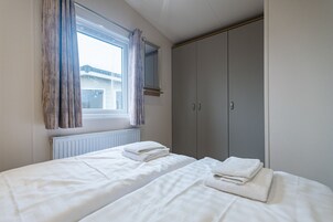 Un dormitorio con dos camas, una ventana con cortinas, un radiador y un armario.