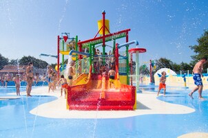 Un parque acuático con una estructura central de juegos acuáticos rodeada por una piscina.