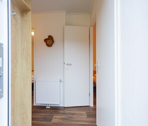 A hallway with a white door, a radiator, and a wooden floor. - Duinhoeve Chalet Zeeland Huisdier Toegestaan (Burgh-Haamstede)