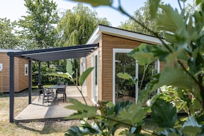 A wooden cabin with a patio area, a table with chairs, and a pergola structure. - Duinhoeve Chalet Zeeland Huisdier Toegestaan (Burgh-Haamstede)