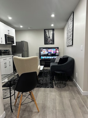 Un salon moderne doté d’un téléviseur à écran plat, d’un canapé et d’un coin repas avec une table et des chaises en verre.