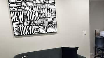 Un salon moderne avec un canapé gris, un coussin à motifs noir et blanc, une table basse en marbre et une œuvre d’art murale représentant un nuage de mots.