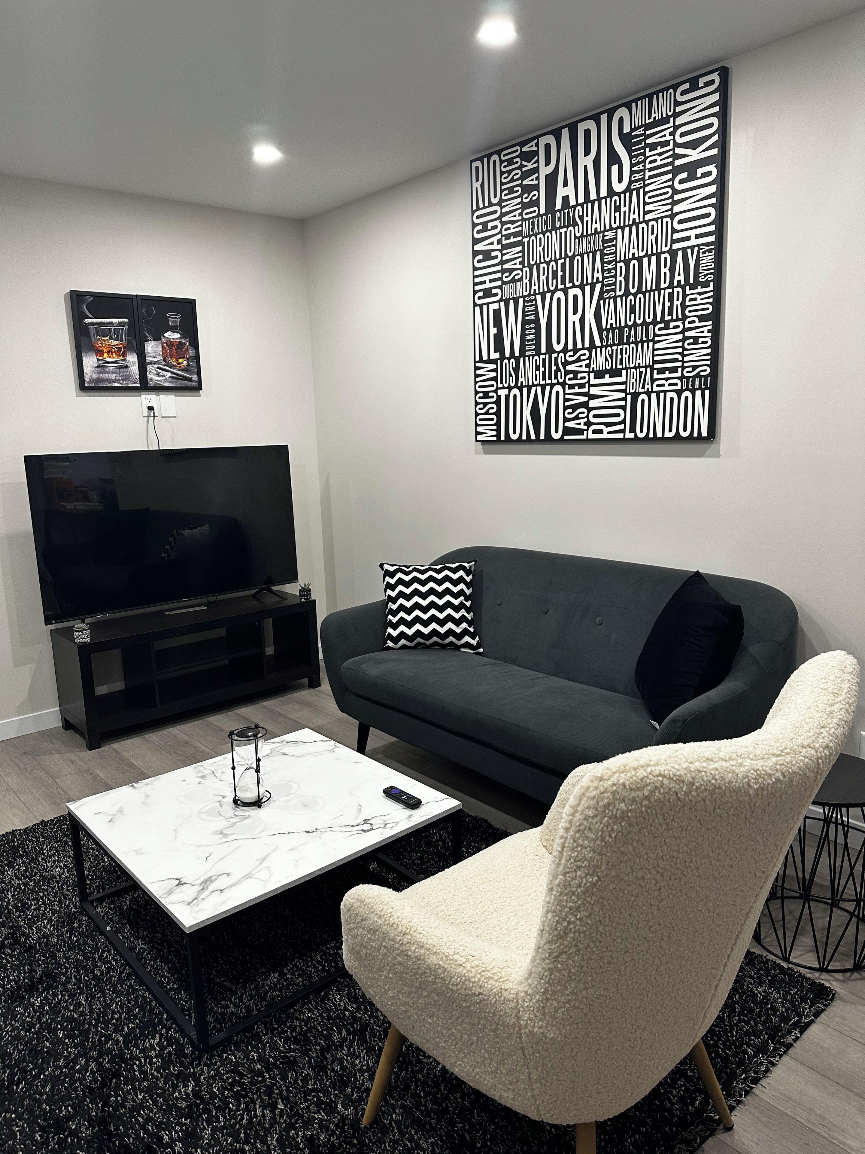 A modern living room with a black sofa, a white armchair, a marble coffee table, and a word cloud wall art piece.