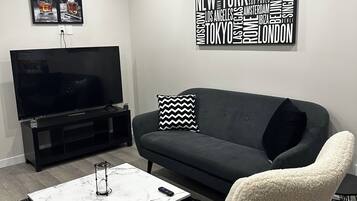 A modern living room with a black sofa, a white armchair, a marble coffee table, and a word cloud wall art piece.