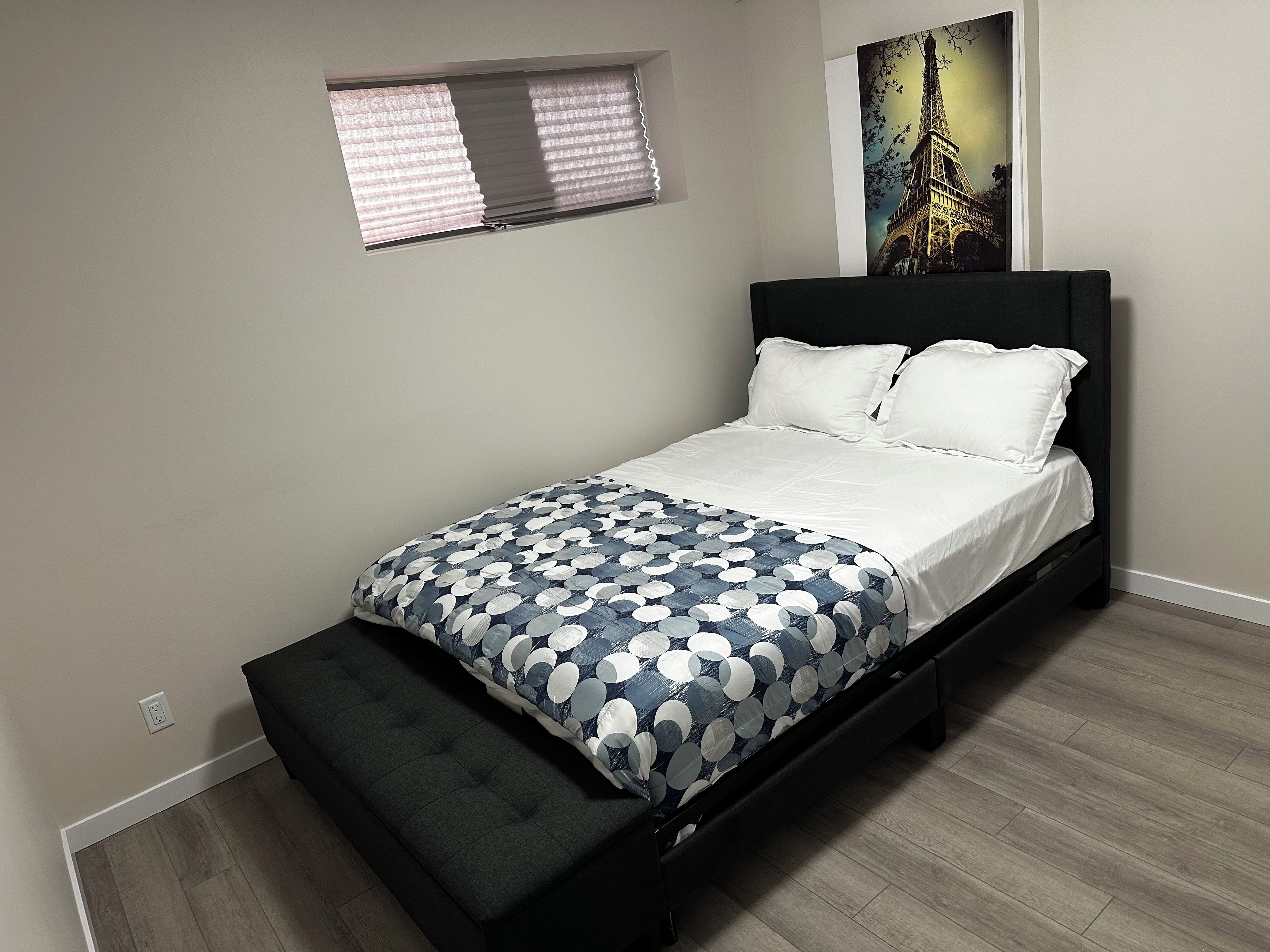 Quarto com uma cama, uma janela e um quadro da Torre Eiffel.