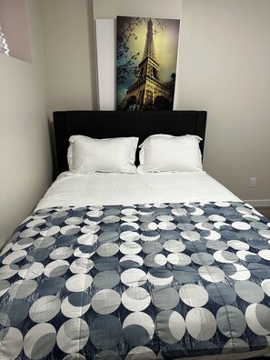 Un lit avec une tête de lit noire, des oreillers blancs et une couvre-lit à motifs bleus et blancs.
