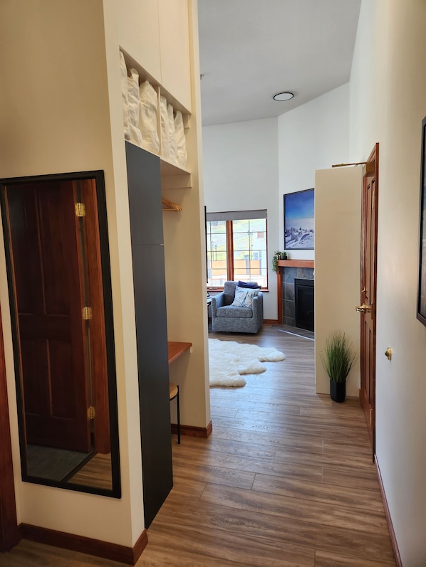 A hallway with a wooden floor, a grey armchair, a white rug, and a plant.