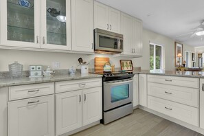 A modern kitchen with white cabinetry, stainless steel appliances, and a granite countertop. - Olde Naples Getaway | 2BR Condo Near Beach & 3rd Ave S (Naples)
