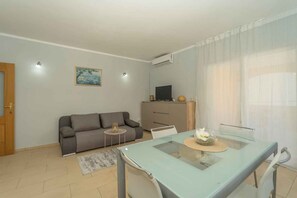 A modern living room with a sofa, a glass dining table, and a television. - Holiday apartment with air conditioning and terrace (Vela Luka)