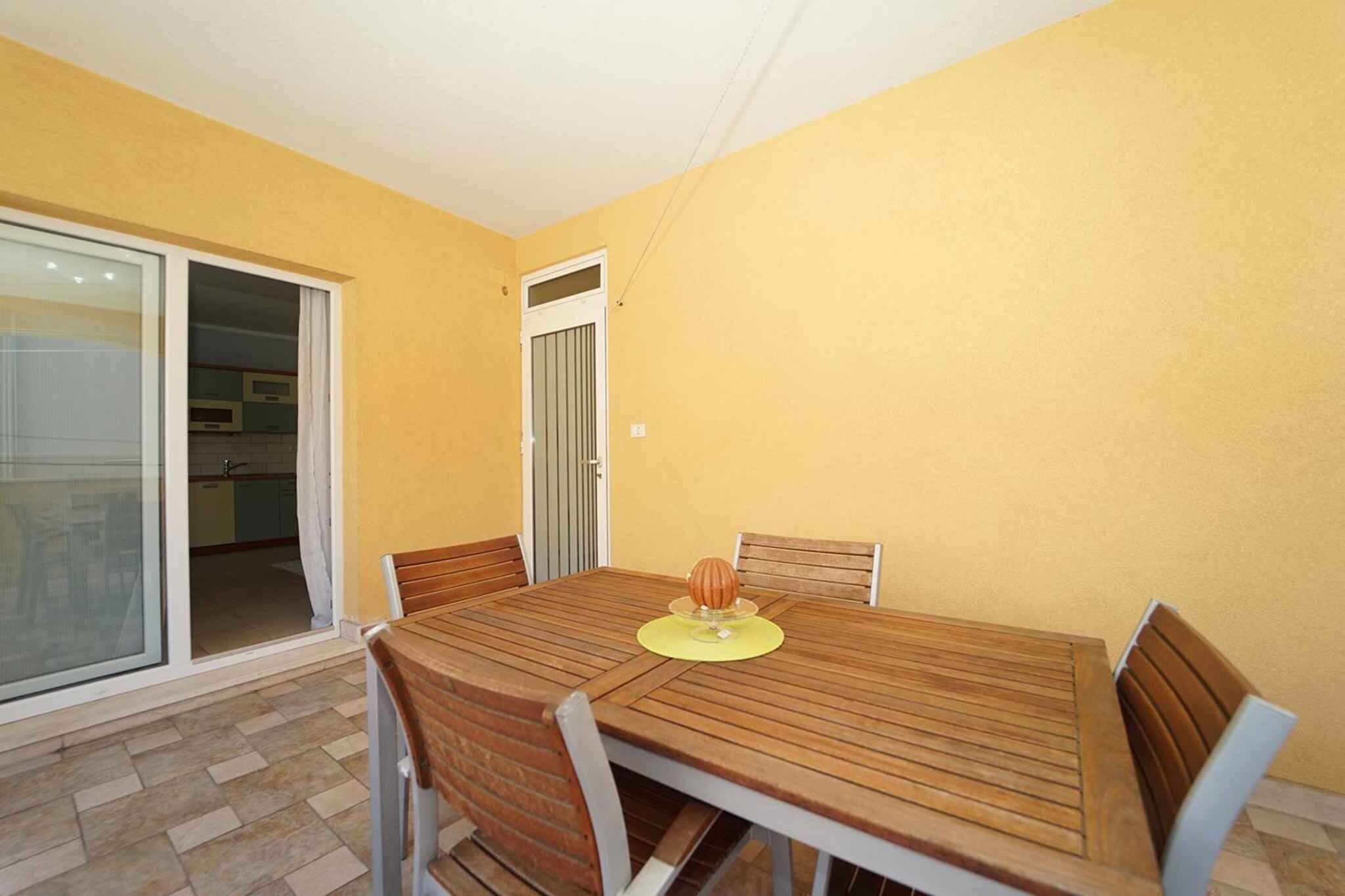 Un coin repas avec une table et des chaises en bois, une porte-fenêtre coulissante donnant sur la cuisine et un mur jaune.