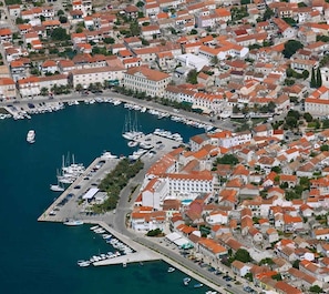 An aerial view of a coastal town with a marina, dense housing, and a prominent white building with a red roof.