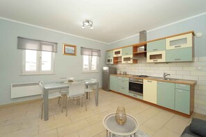 A modern kitchen with a dining area, featuring a central island, built-in cabinets, and a window with blinds.