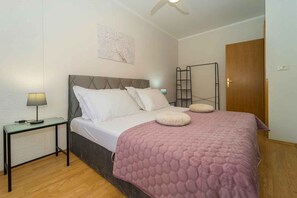 A bedroom with a bed, a nightstand, a lamp, a wall-mounted shelf, and a door. - Holiday apartment with air conditioning and terrace (Vela Luka)