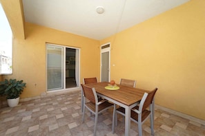 A dining area with a table and chairs, a potted plant, and a sliding glass door leading to a kitchen.
