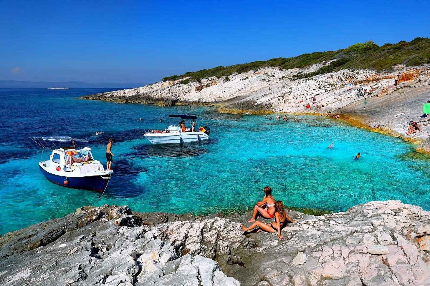 A coastal scene with clear turquoise waters, rocky terrain, and boats.