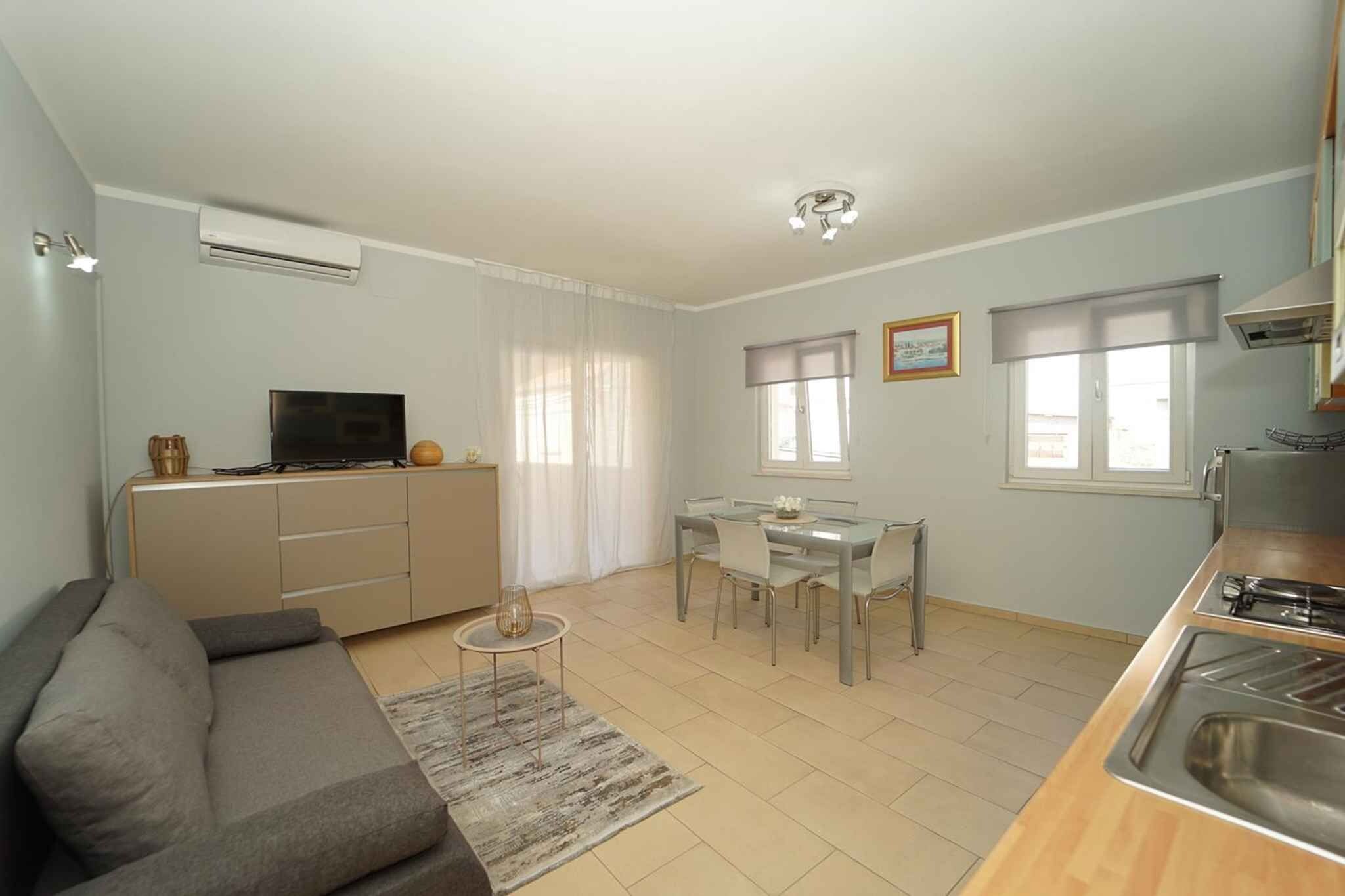 A compact living space with a sofa, a dining table with chairs, a TV, and a kitchenette.