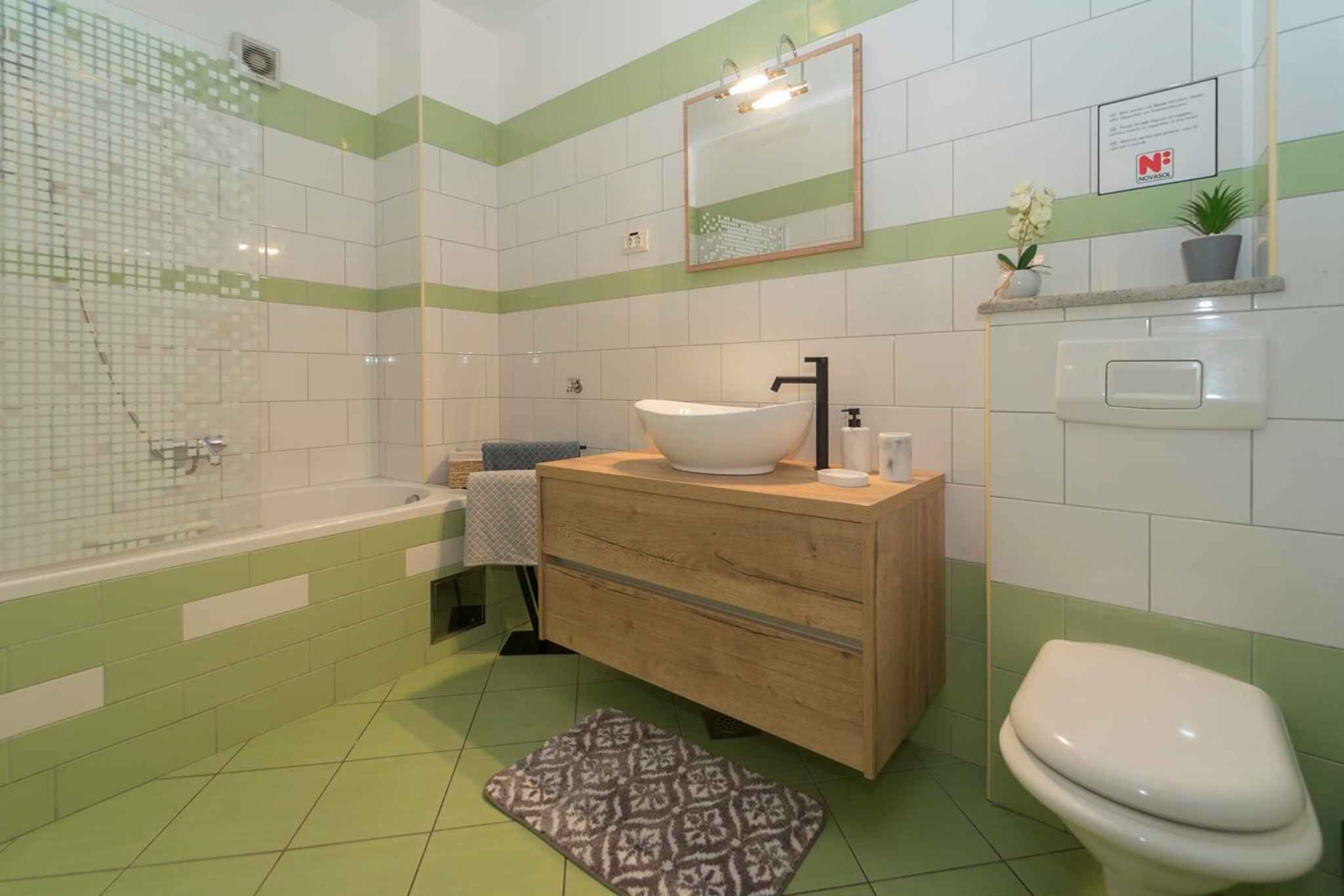 A bathroom with a bathtub, a sink with a mirror, a toilet, and a patterned rug on the floor.