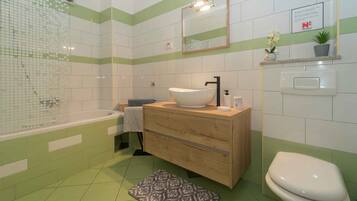 A bathroom with a bathtub, a sink with a mirror, a toilet, and a patterned rug on the floor.