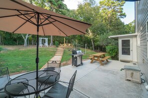Eine Terrasse mit Tisch, Stühlen, Sonnenschirm, Grill und einer Holzterrasse.