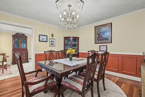 A dining room with a glass-top table, wooden chairs with patterned cushions, a chandelier, and framed artwork on the walls. - Cedar Vista | Mt. Yonah Views & Pool Table (Sautee Nacoochee)