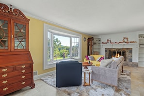 A living room with a fireplace, a large window, and a wooden cabinet. - Cedar Vista | Mt. Yonah Views & Pool Table (Sautee Nacoochee)