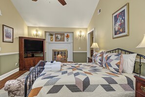 Ein Schlafzimmer mit Kamin, Fernseher, einem Bett mit Steppdecke und einem Gemälde an der Wand.