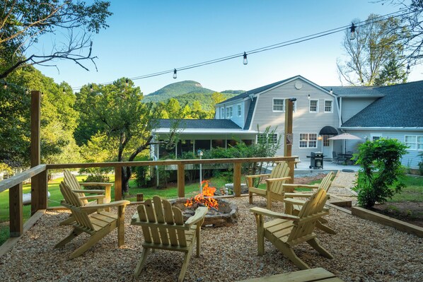A deck with Adirondack chairs and a fire pit, overlooking a house with a mountain backdrop. - Cedar Vista | Mt. Yonah Views & Pool Table (Sautee Nacoochee)