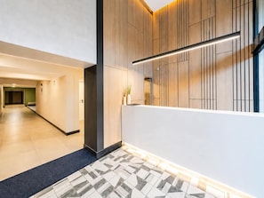 Ein modernes Interieur mit einer Diele, die zu einem Empfangsbereich führt, mit einem geometrischen Muster auf dem Boden, Holzvertäfelung und einer linearen Leuchte.