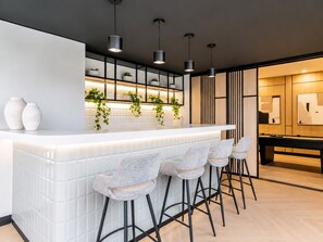 Cozinha moderna com área de bar, armários brancos, plantas penduradas e banquetas.