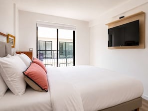 Ein Hotelzimmer mit Bett, einem an der Wand befestigten Fernseher und einem Balkon mit Blick.