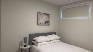 A bedroom with a bed, a bedside table with a lamp, a small plant, and a painting on the wall.