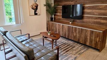 Un salon moderne avec un canapé en cuir, une table basse en bois et un téléviseur à écran plat fixé à un mur en bois.