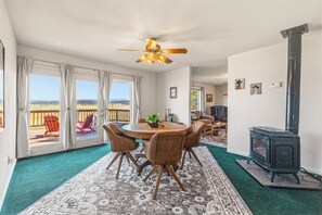 Ein Zimmer mit einem runden Tisch, Stühlen, einem Deckenventilator, einem Kamin und Blick durch große Fenster.