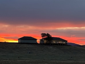 A rural landscape with two buildings on a hill during sunset.