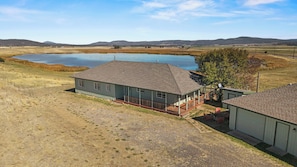 Ein zweigeschossiges Haus mit einem eingezäunten Garten, einem Teich und einer hügeligen Landschaft im Hintergrund.