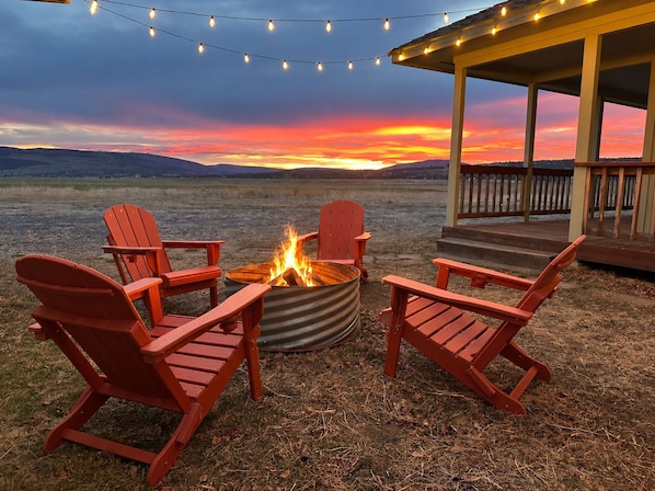 An outdoor seating area with red chairs and a fire pit, under a covered structure with string lights.